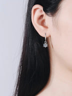 Close-up of an ear wearing a silver earring with a clear gemstone on a plain background