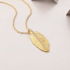 Gold feather pendant necklace with pavé moissanite detailing on a delicate chain displayed on a soft neutral background