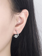 Close-up of an ear wearing a silver earring with a clear gemstone.