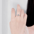 Hand wearing a silver ring with a green gemstone on a light gray background