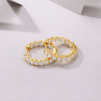 Pair of gold hoop earrings with clear gemstones on a light pink background