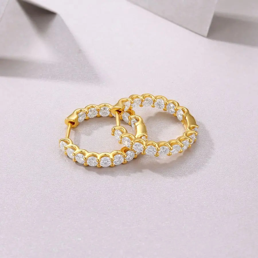 Pair of gold hoop earrings with clear gemstones on a light pink background