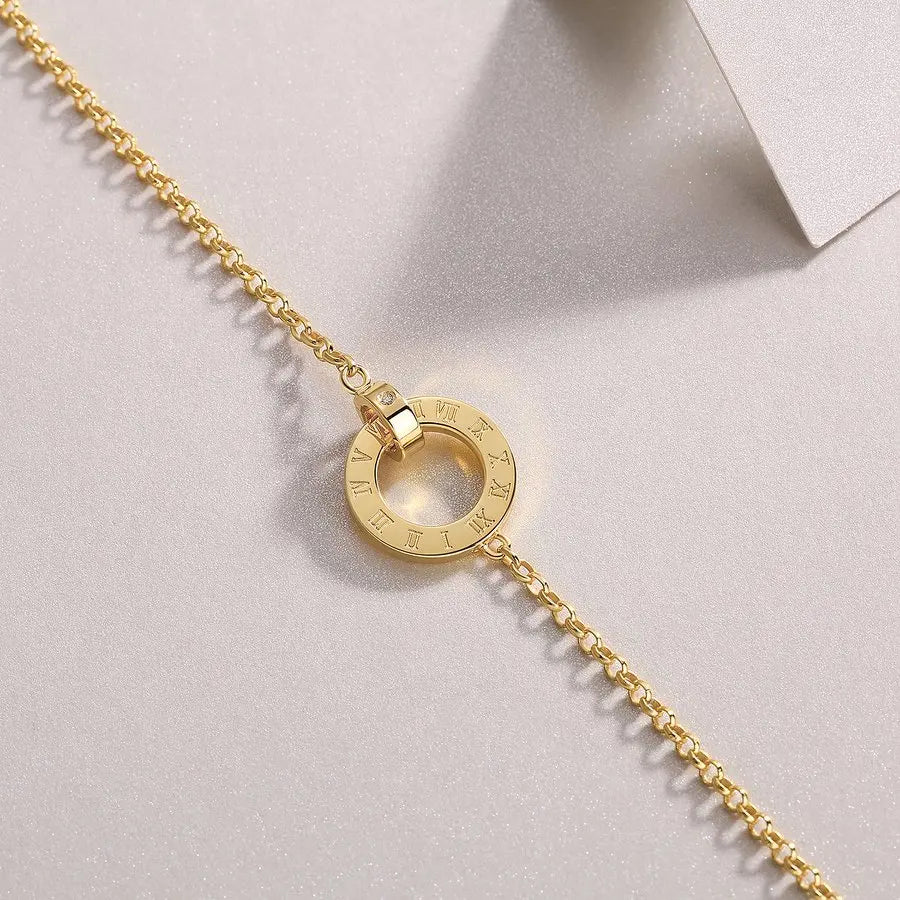 Gold bracelet with a circular clasp on a light gray background