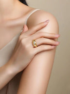 Gold signet-style ring with a bezel-set moissanite stone worn on a model’s hand against a soft neutral background