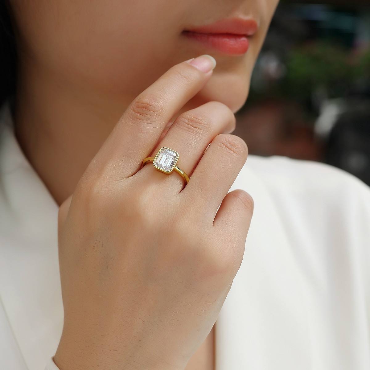 Close-up of a hand wearing a gold ring with a diamond on a blurred background