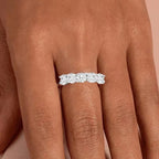 Silver ring with diamonds on a person's finger against a neutral background