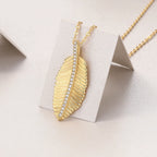 Gold feather-shaped necklace with embedded stones on a light gray background