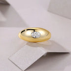 Gold signet-style ring with a bezel-set round moissanite stone displayed on a soft neutral background