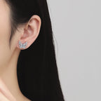 Close-up of an ear wearing a silver earring with gemstones on a neutral background