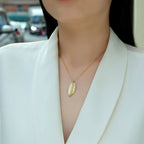 Gold feather pendant necklace worn on a model, featuring pavé moissanite detailing on a delicate chain