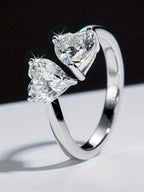 Silver ring with two heart-shaped diamonds on a reflective surface