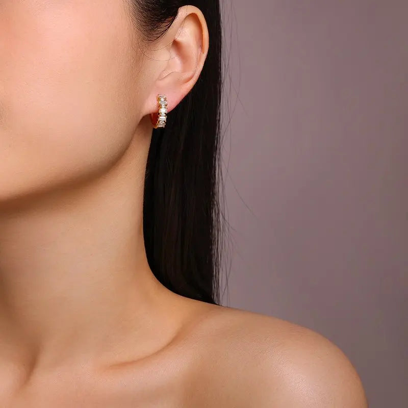 Close-up of a person wearing a diamond hoop earring against a neutral background