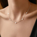Silver necklace with small beads on a person's neck against a neutral background