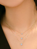 Close-up of a person wearing two gold necklaces with blue gemstones on a blurred background