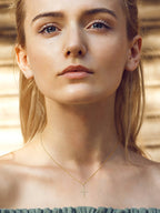 Close-up of a woman wearing a gold necklace with a cross pendant against a blurred natural background.