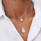 Two silver necklaces with pendants on a person wearing a white shirt.