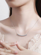 Necklace with a subtle design worn by a person in a delicate outfit.