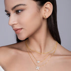 Woman wearing gold necklaces and earrings on a neutral background