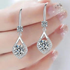 Silver teardrop earrings with clear gemstones held by a hand against a light background