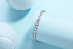 White gold bezel-set tennis bracelet with round brilliant stones, photographed on a soft blue background