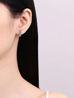 Close-up of a person wearing a silver hoop earring against a light purple background
