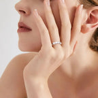 Close-up of a woman's hand wearing a diamond ring, with a soft focus on her face.