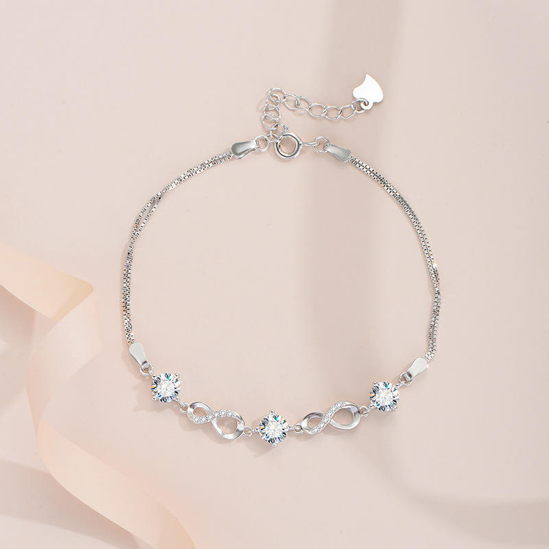 Silver bracelet with heart and infinity symbol charms on a beige background