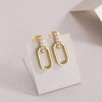 Gold earrings with clear stones on a white card against a light gray background