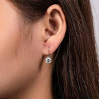 Close-up of an ear wearing a diamond earring with dark hair and skin background