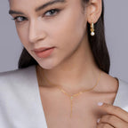Woman wearing a gold necklace and earrings against a neutral background