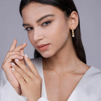 Woman wearing gold jewelry including earrings, necklace, and ring on a gray background