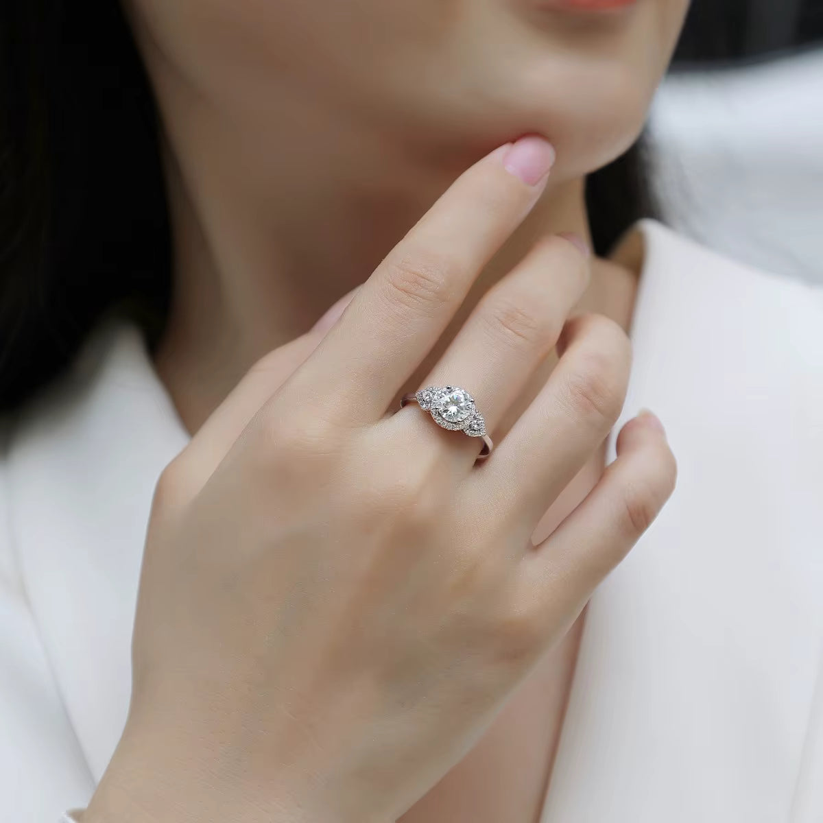 Close-up of a hand wearing a silver ring with a diamond, against a neutral background.