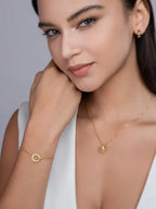 Woman wearing gold jewelry including a necklace and bracelet against a neutral background