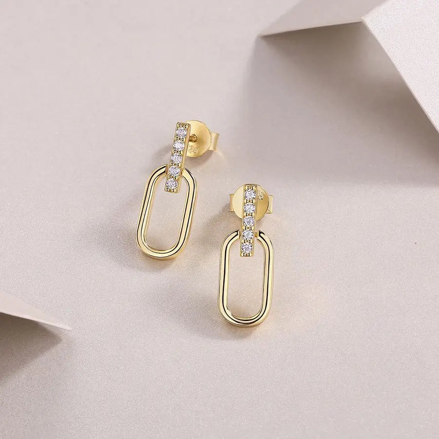 Gold hoop earrings with embedded stones on a light pink background