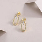 Gold hoop earrings with embedded stones on a light pink background