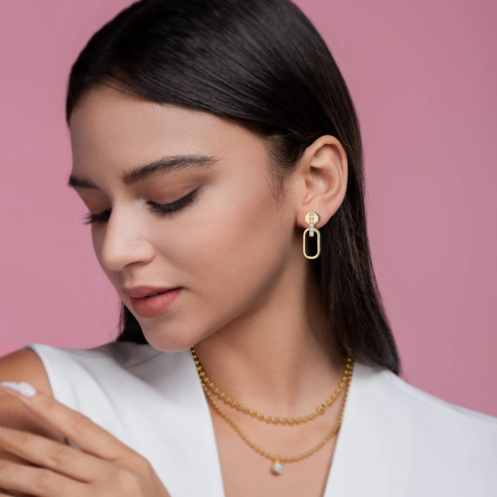 Woman wearing gold earrings and necklaces against a pink background