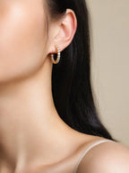Close-up of a person wearing gold hoop earrings with a neutral background