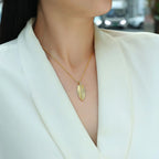 Person wearing a gold necklace with a leaf pendant against a blurred background
