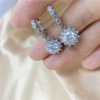 Silver hoop earrings with star-shaped diamond pendants on a hand.