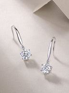 Pair of silver earrings with clear gemstones on a beige background