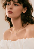 Woman wearing a delicate necklace with a small pendant against a neutral background