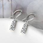 Silver teardrop earrings with clear gemstones on a soft fabric background