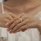 Close-up of a hand wearing a gold ring with gemstones on a neutral background