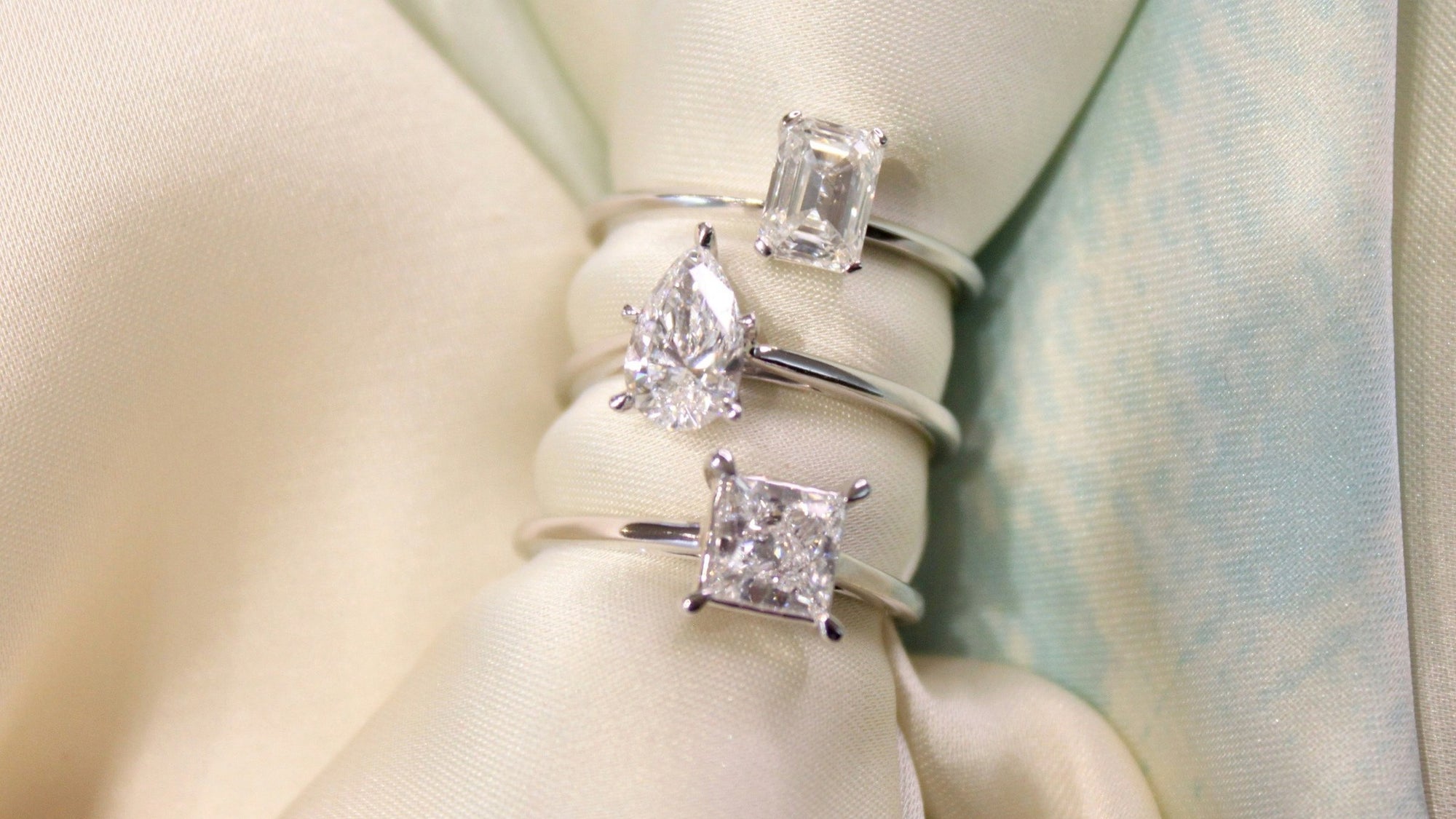 Three diamond rings stacked on a soft fabric background